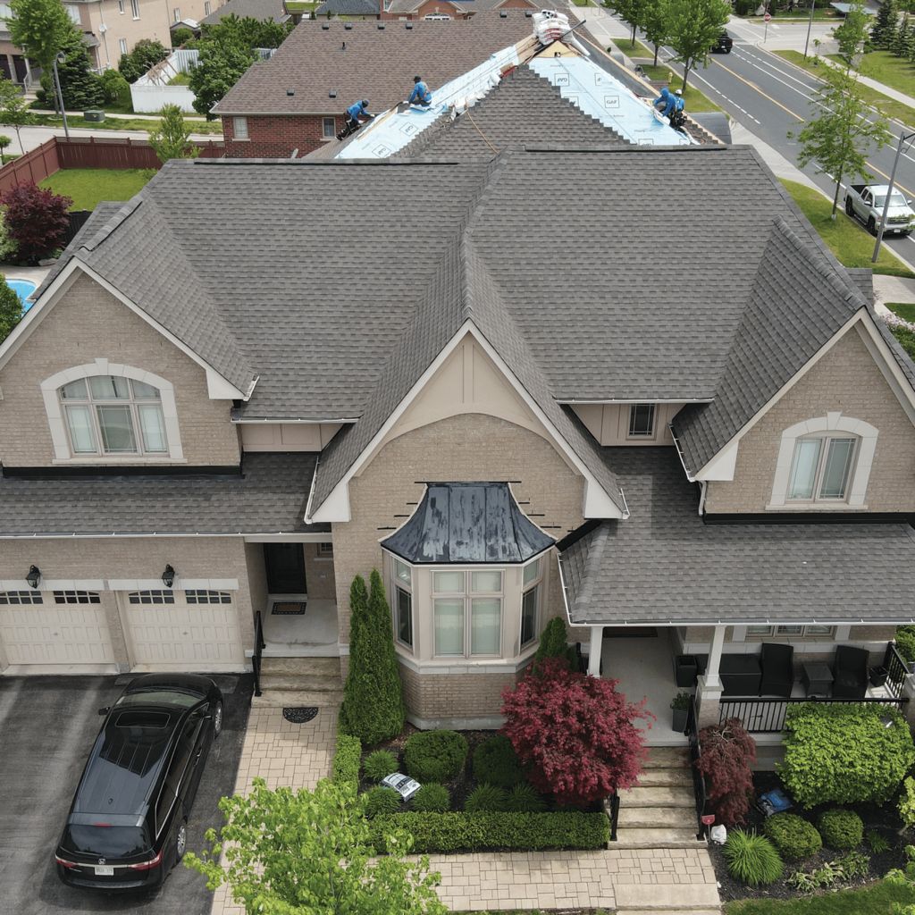 Aerial view of roofers installing asphalt shingles on a brick home, about to complete a roofing project by The Roofers in Markham