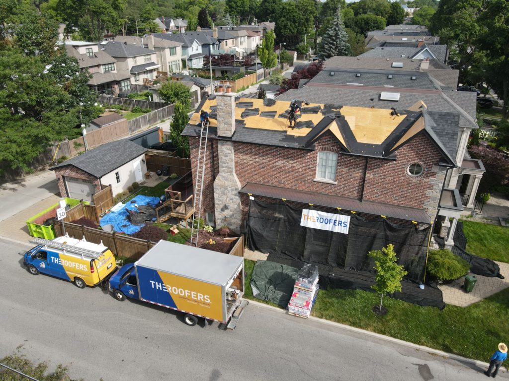 Aerial view of a brick home with workers installing shingles, completing a roofing project by The Roofers in Toronto